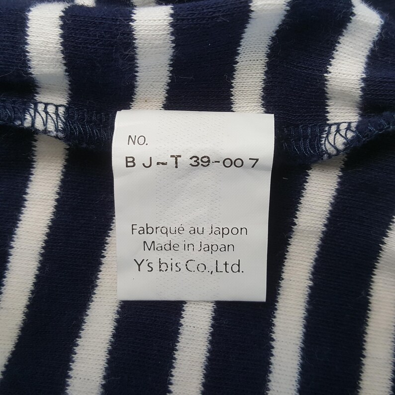 May include: Close-up of a navy blue and white striped fabric with a tag. The tag reads "NO. B J~T 39-007" and "Fabriqu&eacute; au Japon Made in Japan Y's bis Co.,Ltd."