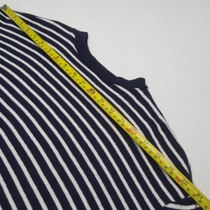 May include: A navy blue and white striped sleeveless top. The top is measured with a yellow tape measure. The stripes are vertical and evenly spaced. The top is made of a knit fabric.