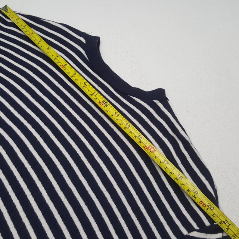 May include: A navy blue and white striped sleeveless top. The top is measured with a yellow tape measure. The stripes are vertical and evenly spaced. The top is made of a knit fabric.