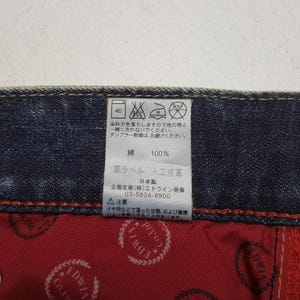 May include: Close-up of a tag on denim fabric. The tag includes washing instructions, fabric composition (100% cotton), and a warning about color transfer. The tag also has Japanese text.