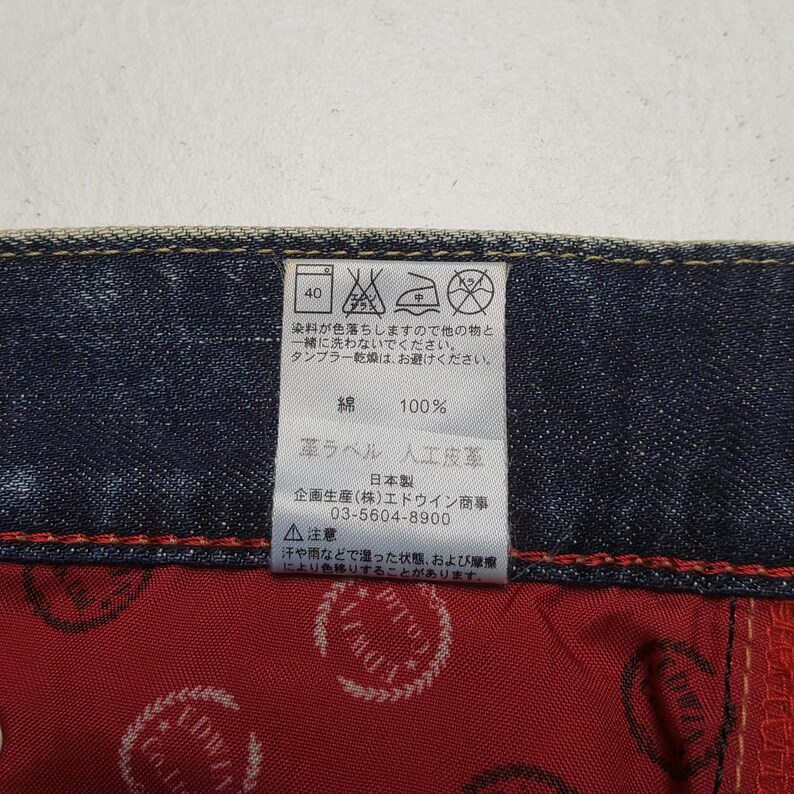 May include: Close-up of a tag on denim fabric. The tag includes washing instructions, fabric composition (100% cotton), and a warning about color transfer. The tag also has Japanese text.