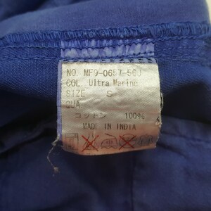 May include: Close-up of a blue garment with a tag. The tag reads "NO. MF9-0657-56J COL. Ultra Marine SIZE S". The tag also indicates the material is 100% cotton and "MADE IN INDIA".