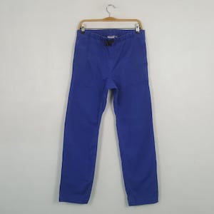 May include: A pair of solid blue pants hanging on a wooden hanger. The pants have a drawstring waist and a straight leg design. The fabric appears to be a medium-weight cotton or blend.
