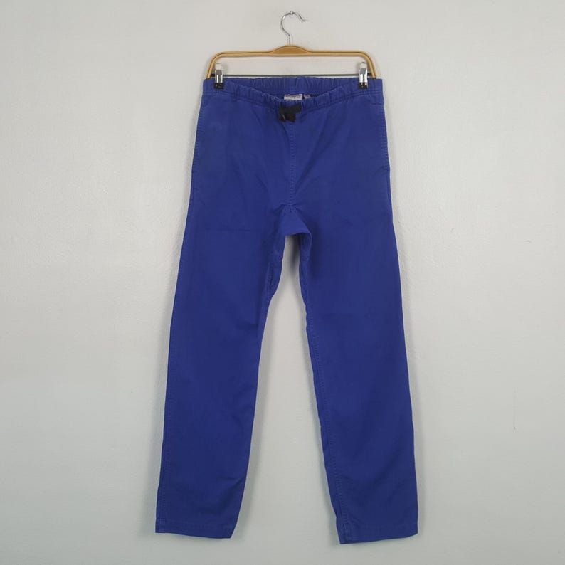 May include: A pair of solid blue pants hanging on a wooden hanger. The pants have a drawstring waist and a straight leg design. The fabric appears to be a medium-weight cotton or blend.