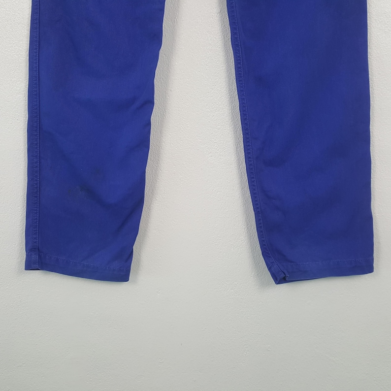 May include: A pair of vibrant blue pants. The pants are made of a solid, smooth fabric and feature visible stitching along the seams. The image shows the lower portion of the pants, from the knees down.