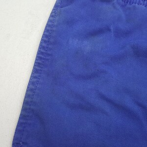 May include: Close-up of a section of blue fabric with visible diagonal lines and a stitched seam. The fabric is a solid, vibrant blue color, with a slightly textured appearance. The seam is on the left side of the image.
