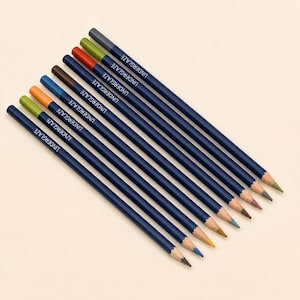 May include: A set of nine dark blue pencils with the word UNDERGLAZE printed in white on each barrel. Each pencil features a different coloured tip, including shades of green, orange, blue, brown, red, and grey, arranged in a diagonal row.