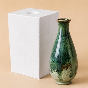 May include: A white rectangular plaster mold with a circular opening at the top and a teardrop-shaped ceramic vase featuring a glossy glaze in shades of forest green, emerald, and light cream with a speckled texture and a narrow neck.