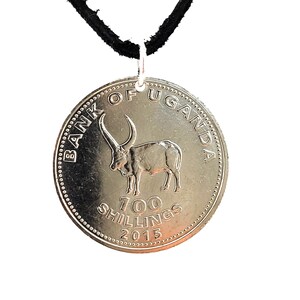 May include: A silver pendant featuring a Ugandan 100 Shillings coin from 2015, with a long-horned Ankole-Watusi bull design. The coin is suspended from a black cord necklace. The coin reads "BANK OF UGANDA" and "100 SHILLINGS".
