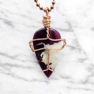 May include: A copper wire wrapped pendant featuring a purple and white gemstone. The pendant is shaped like a teardrop and hangs from a copper chain.