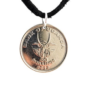May include: A silver coin necklace featuring a Ugandan 50 shilling coin from 2012. The coin depicts an antelope with large horns and the text "BANK OF UGANDA 50 SHILLINGS 2012".