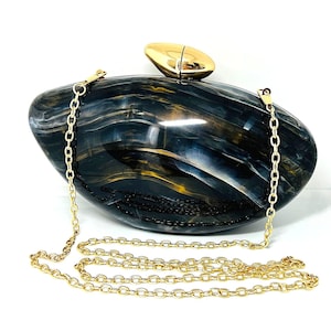 Könnte beinhalten: Ovale Clutch-Tasche mit Marmoreffekt in Marineblau, Gold und Weiß. Sie hat einen goldfarbenen Verschluss und eine Kette. Die Kette ist an den Seiten der Tasche befestigt. Maße ca. 20 cm lang.