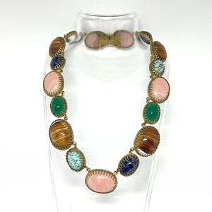 Könnte beinhalten: Ein Vintage-Halsketten- und Armband-Set. Die Halskette besteht aus ovalen Steinen in verschiedenen Farben, darunter Rosa, Grün, Blau und Braun, die in einem goldfarbenen Metallrahmen gefasst sind. Das Armband spiegelt das Design der Halskette wider.