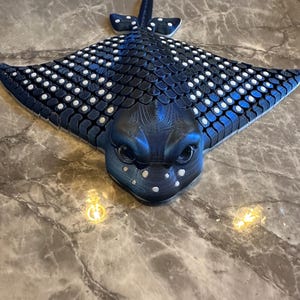 May include: A blue and white 3D printed stingray sculpture with a textured surface and white spots. The stingray is facing forward with its mouth open.