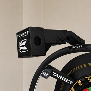 May include: A black Target brand dartboard lighting system featuring a rectangular camera housing with the Target logo and text, mounted on a circular frame that extends over a dartboard with visible numbers 12, 9, 14, and 5 in a black colour scheme.