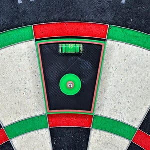 May include: A dartboard with the word "TARGET" at the top. The board has a black center with a green bullseye and a level tool. The board has red, green, and white sections. The level tool is used to ensure the board is straight.