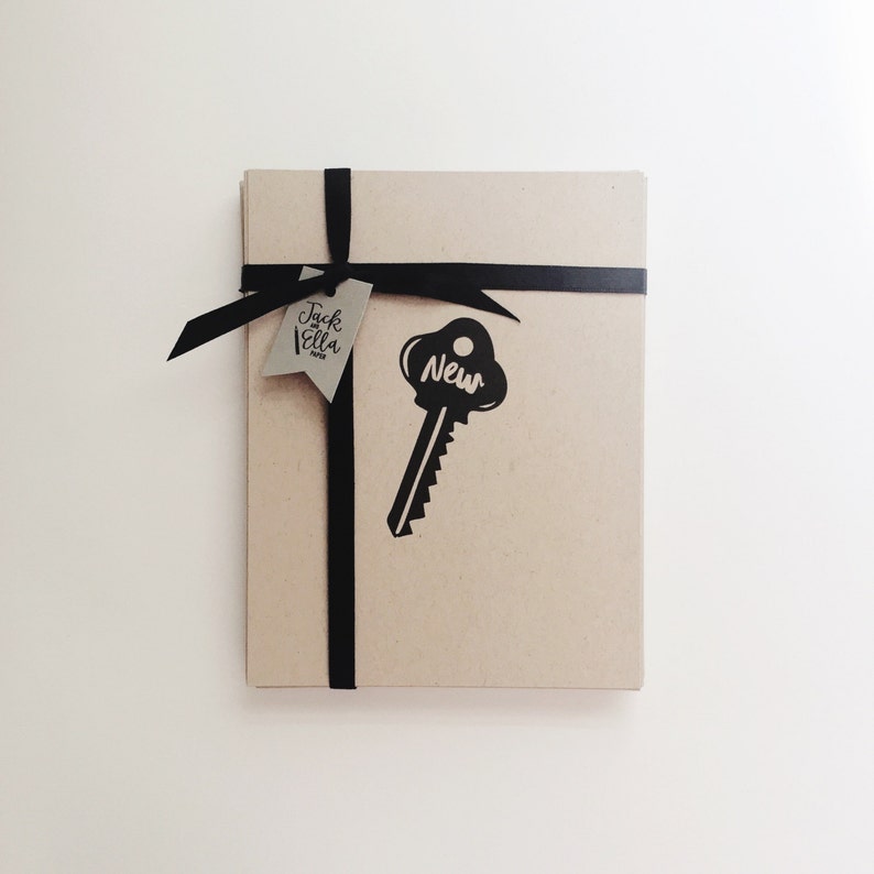 May include: A brown gift box wrapped with black ribbon and a tag that says "Jack & Ella Home". A black key-shaped sticker with the word "New" is on the box.