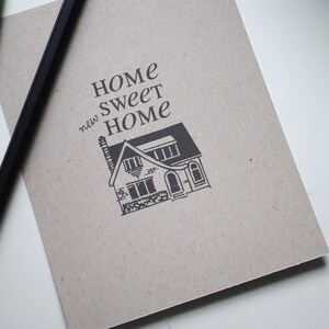 May include: A brown paper notebook with the text "Home Sweet new Home" and a black and white illustration of a house.