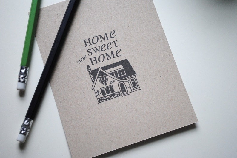 May include: A brown paper notebook with the text "Home Sweet new Home" and a black and white illustration of a house.