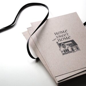 May include: A stack of brown paper cards with a black ribbon tied around them. The cards have the text "Home Sweet Home" printed on them with a small illustration of a house.