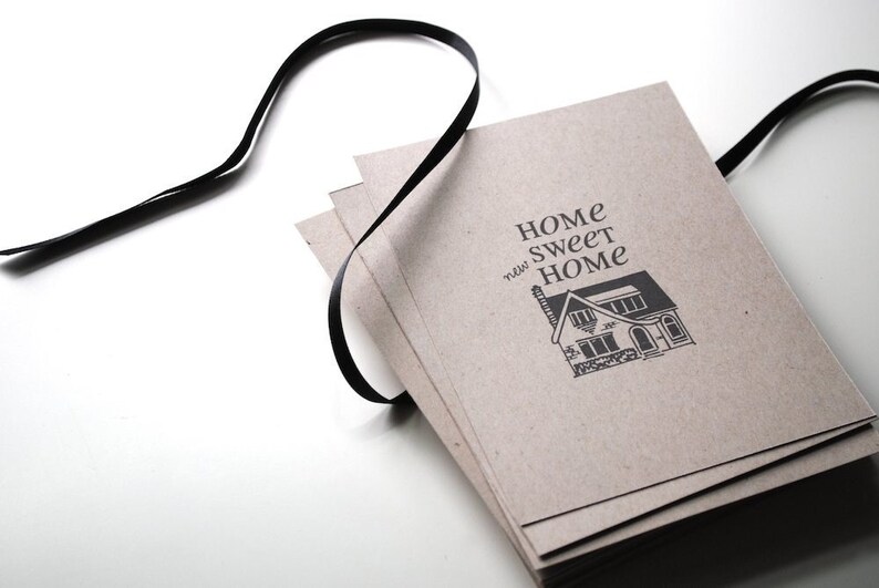 May include: A stack of brown paper cards with a black ribbon tied around them. The cards have the text "Home Sweet Home" printed on them with a small illustration of a house.