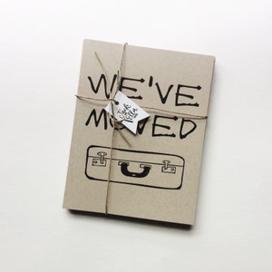 May include: A brown card with the text "WE'VE MOVED" in black handwritten font. A small white tag with the text "Jack & Ella" is tied to the card with twine.