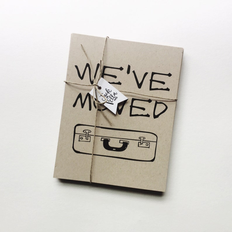 May include: A brown card with the text "WE'VE MOVED" in black handwritten font. A small white tag with the text "Jack & Ella" is tied to the card with twine.