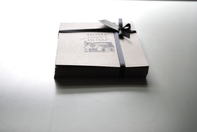 May include: A stack of brown paper cards tied with a black ribbon. The cards have a black and white illustration of a house with the text "Home Sweet Home" printed on the front.