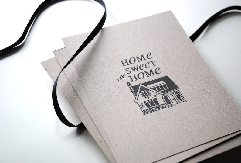 May include: A stack of brown cards with a black ribbon tied around them. The top card has the text "HOME sweet new HOME" and a black and white illustration of a house.
