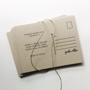 May include: A stack of brown kraft paper postcards with a twine string tied around them. The front of the postcard has the text "PLEASE UPDATE YOUR CONTACTS :)" and "JAROD & JENNY MILLER 3200 SUNRISE LANE SANTA CRUZ, CA 95064 KEEP IN TOUCH!" The back of the postcard has a white rectangle for the address and the text "www.jackandellapaper.com" and "jack+ella PAPER".