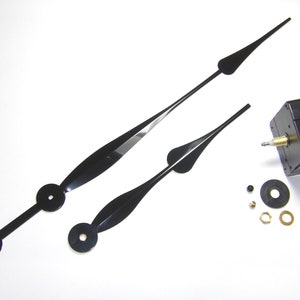 Könnte beinhalten: Schwarze Uhrzeiger und ein Uhrwerk-Set. Das Set enthält zwei Uhrzeiger, ein Uhrwerk, eine Unterlegscheibe, eine Mutter und ein kleines Metallstück.