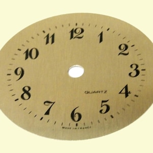 Puede incluir: Una esfera de reloj de color dorado con números y manecillas negros. La esfera está marcada con "QUARTZ" y "MADE IN FRANCE".