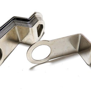 May include: A collection of silver-colored metal derailleur hangers featuring a Z-shaped profile with a circular mounting hole on one end and a triangular aperture on the opposite end. The components are made of a smooth, reflective metallic material.