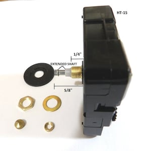 May include: Black clock movement with a 5/8 inch extended shaft and a 1/4 inch shaft. The movement is labeled HT-15. The image also shows a black washer, two gold-colored washers, a gold-colored nut, and a gold-colored pin.