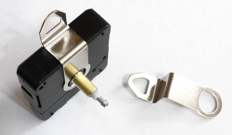 May include: A black clock movement with a silver metal bracket and a separate silver metal bracket with a hole. The clock movement has a gold-colored shaft with a white tip.