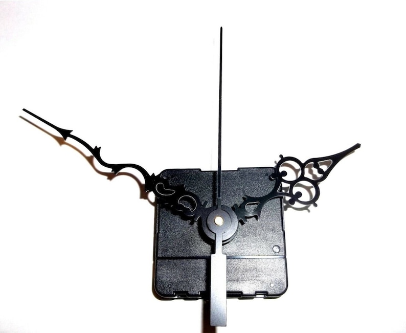 May include: Black clock hands with a decorative design. The hands are attached to a black plastic clock movement.