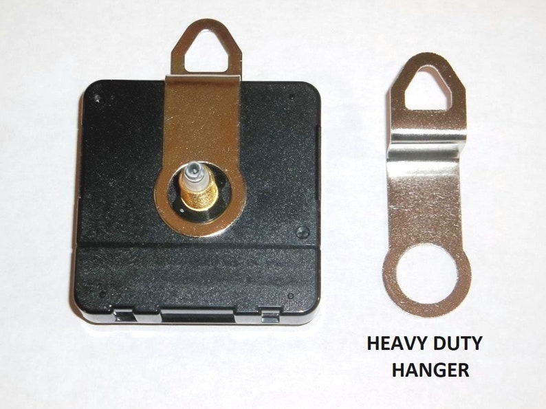 May include: A black clock movement with a gold-colored hanger. The movement has a small hole in the center for the clock hand. The hanger is labeled "Heavy Duty Hanger".
