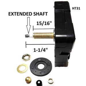 May include: Black clock movement with an extended shaft, labeled "HT31" and "EXTENDED SHAFT". The shaft measures 1-1/4" long and 15/16" in diameter. The movement comes with a black plastic gear, a gold washer, a gold nut, a gold crown, a black crown, and a gold washer.