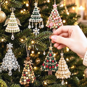 May include: A collection of decorative Christmas tree ornaments featuring various designs including beaded cone shapes, angel figures with wings, and star toppers. The ornaments are crafted with pearls, crystals, and colourful beads, hanging from strings on a pine tree.