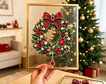 May include: A decorative Christmas wreath inside a gold rectangular frame, featuring green foliage, red and white pearls, large red faceted gems, and a prominent red bow at the top with a dangling red teardrop gem at the bottom center.