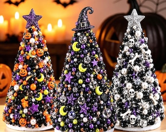 Op de afbeelding: Drie kegelvormige decoratieve bomen bedekt met kralen en bedels. De linkerboom heeft oranje pompoenen en een paarse ster. De middelste boom heeft een heksenhoed, manen en sterren. De rechterboom toont witte schedels en botten met een zilveren ster.
