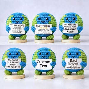 May include: Six crocheted globe-shaped ornaments, each with a smiling face and holding a sign. The signs display various messages, including "To My Love," "Best Friend," and "Dad." The globes are blue and green, with wooden bases.