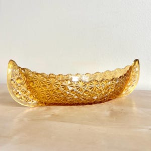 Könnte beinhalten: Eine bernsteinfarbene, längliche Glasschale mit einem dekorativen Sternmuster. Die Schale hat einen gewellten Rand und gebogene, kanuförmige Enden. Das Glas hat ein strukturiertes, rautenförmiges Muster.