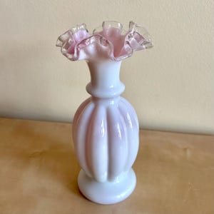 Può includere: Un vaso vintage in vetro rosa pallido e bianco. Presenta un bordo a balze, un corpo bulboso con scanalature verticali e una base rotonda. Il bordo e l'interno sono rosa chiaro, il corpo bianco con sfumature rosa. Decorativo.
