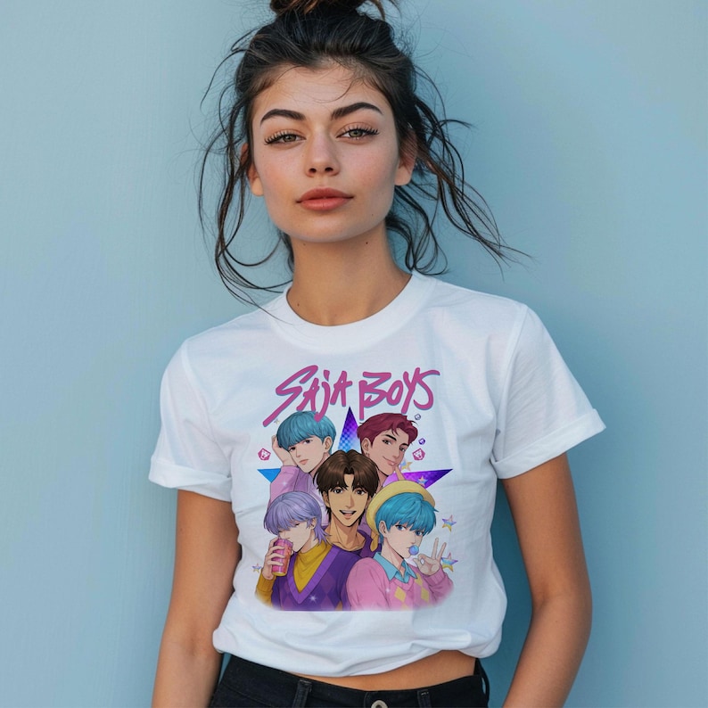 May include: White t-shirt featuring a graphic of six anime-style characters with colorful hair, the text "Suit Boys" in pink and purple, and a star design. The shirt is worn by a person against a light blue background.