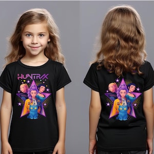 May include: Black t-shirt featuring a graphic design with the text "HUNTRAX" and a star-shaped design with illustrations of women and a blue cat. The shirt is worn by a young person.