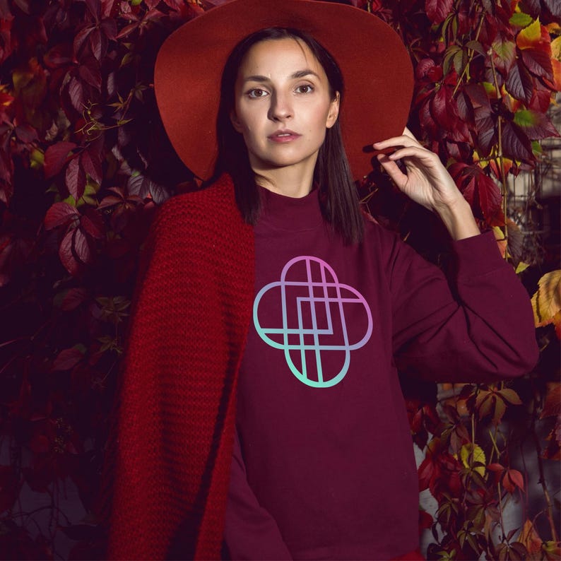 K&ouml;nnte beinhalten: Ein weinrotes Sweatshirt mit einem geometrischen Design in Rosa und T&uuml;rkis. Ein roter Hut und Schal sind ebenfalls zu sehen. Der Hintergrund zeigt weinrote Bl&auml;tter.
