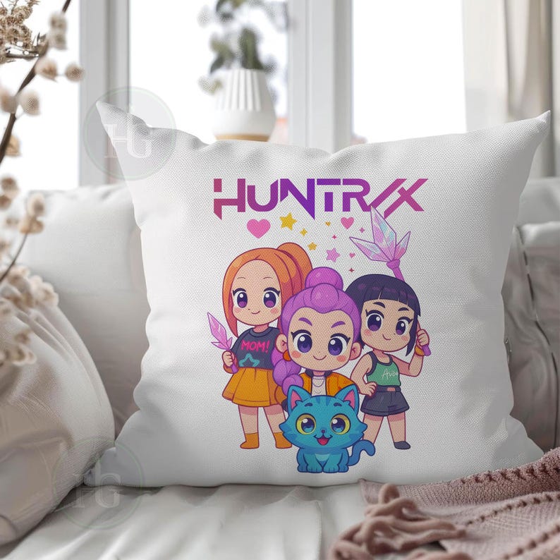 Pu&ograve; includere: Cuscino decorativo bianco con una grafica a cartoni animati colorata. Il design include tre figure stilizzate, un gatto blu e la scritta "HUNTRAX" in viola. Le figure tengono in mano oggetti simili a cristalli.