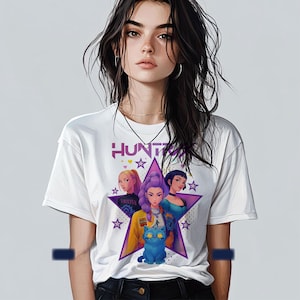 May include: White t-shirt featuring a graphic of three women and a blue cat inside a purple star. The word "HUNT" is printed above the star. The women are in various outfits, and the cat has large eyes.