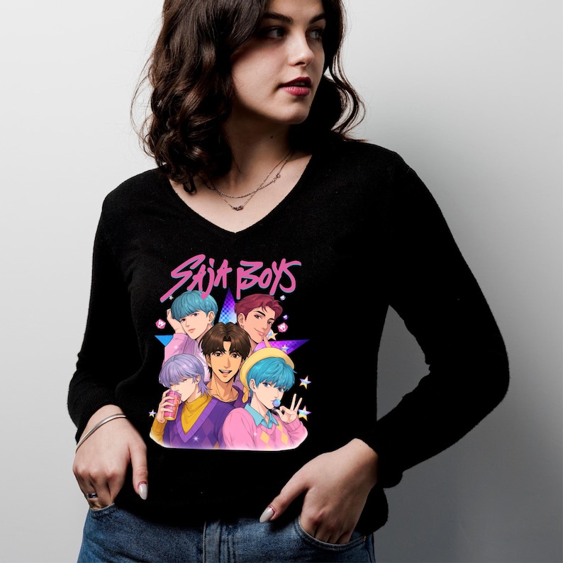 May include: Black long-sleeve V-neck shirt featuring a graphic of six cartoon figures with colorful hair and the text "Saja Boys" in pink and blue. The figures are set against a purple star background.